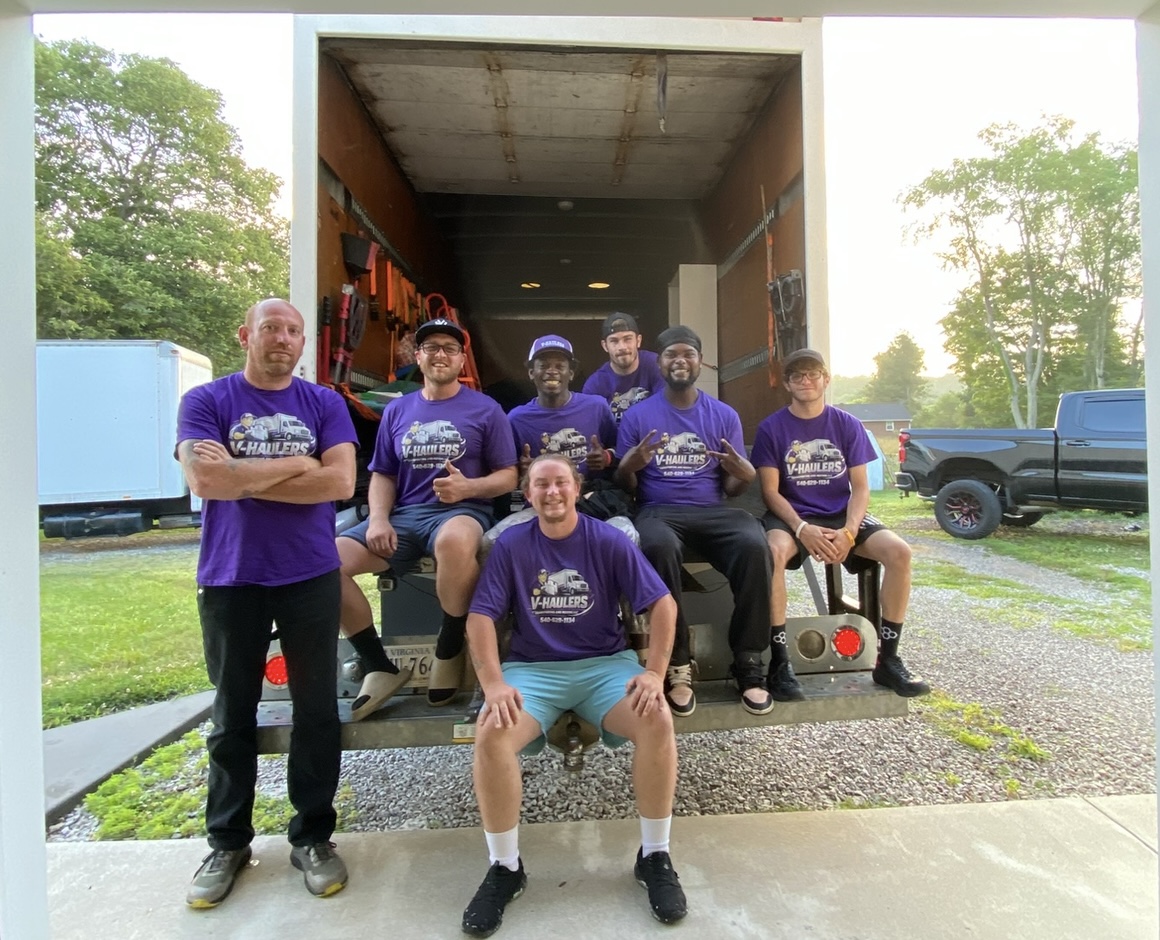 The V-Haulers crew in purple hoodies sitting on the tailgate of their moving truck