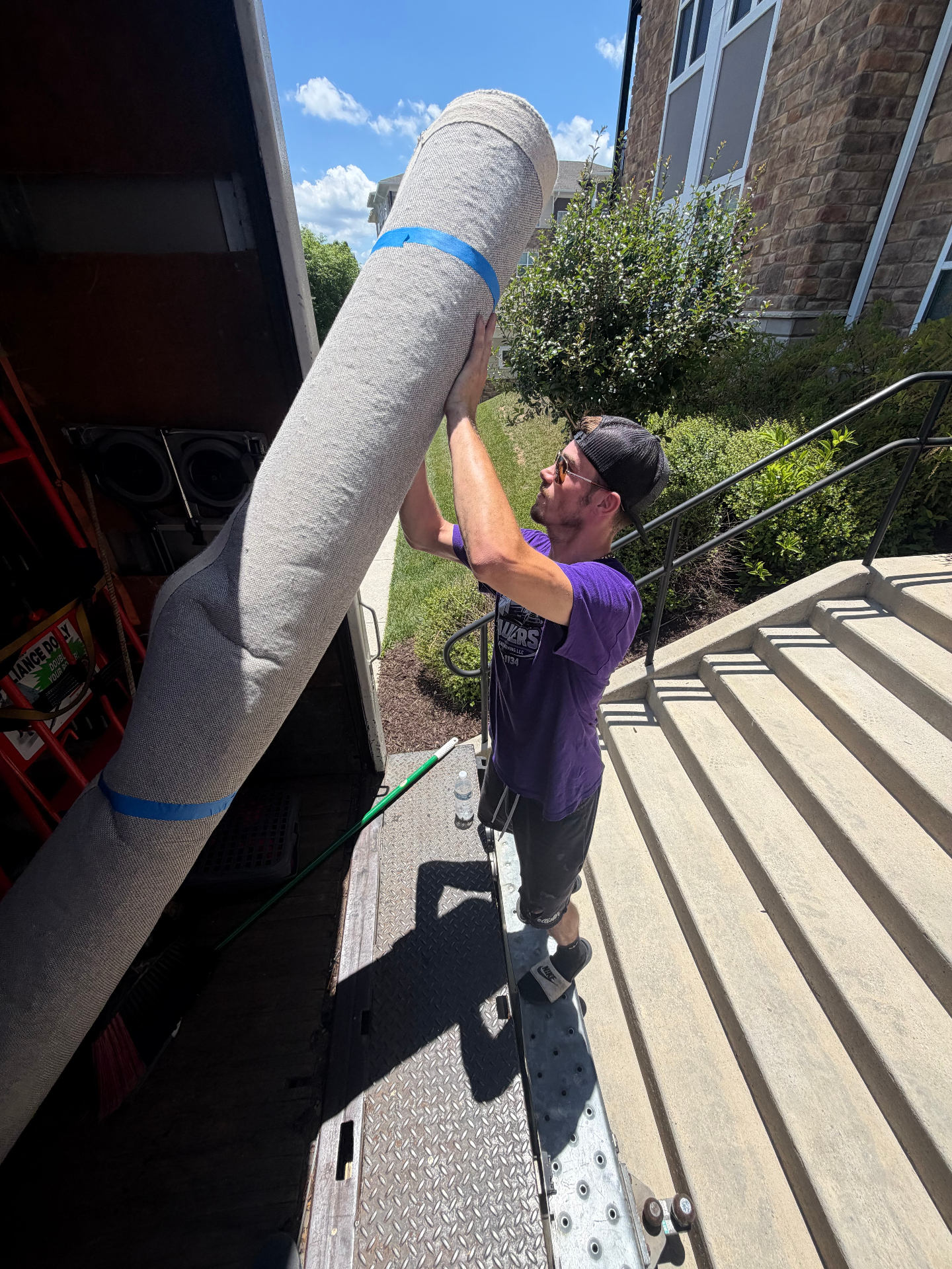 V-Haulers mover in purple shirt loading a wrapped rug into the moving truck